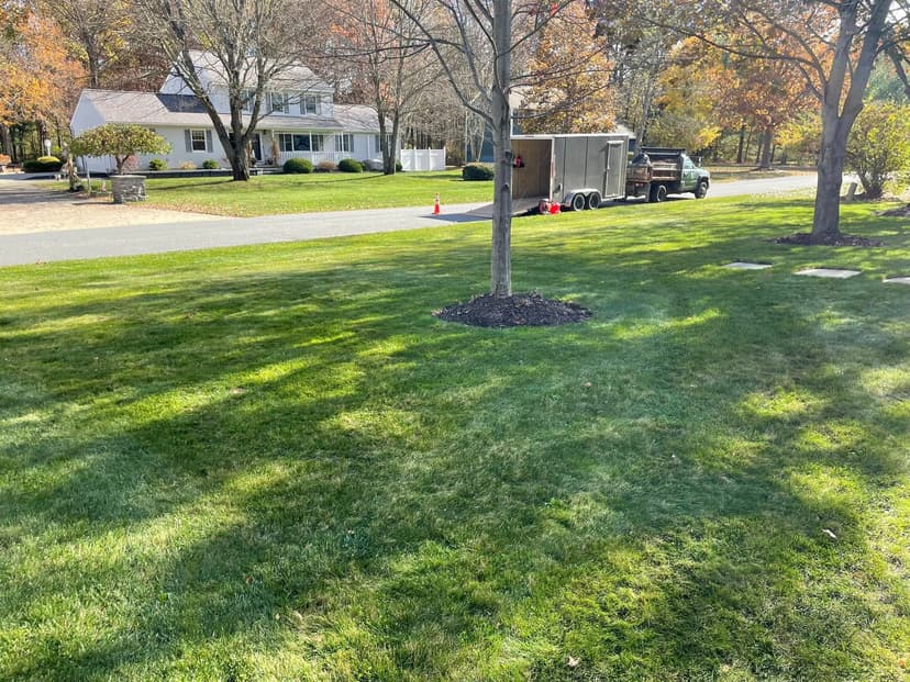 Lawn maintenance truck parked near a suburban home with autumn foliage.